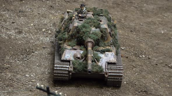 An Exhibition of Army Car Models. A Camouflaged Tank Drives and Turns on a Model Dirt Road.