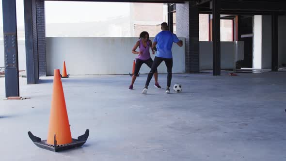 African american man and woman playing football in an empty urban building