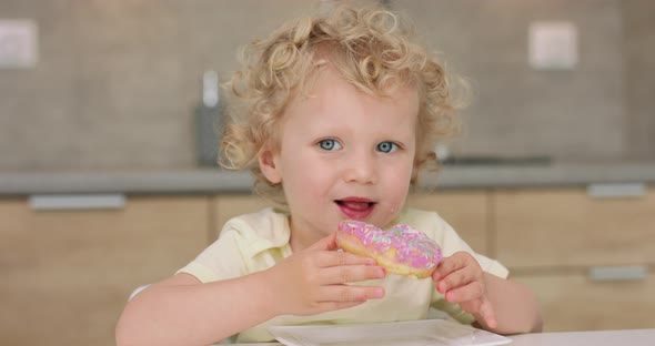 Adorable Little Girl Looks to the Left Then Takes a Donut From the Plate and Bites While Sitting at