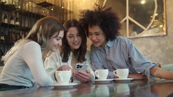 Three Multiethnic Young Women in a Coffee Shop Looking at the Phone