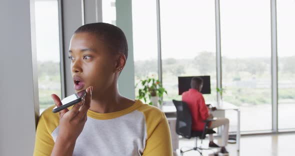 African american creative businesswoman talking on smartphone, with male colleague in background