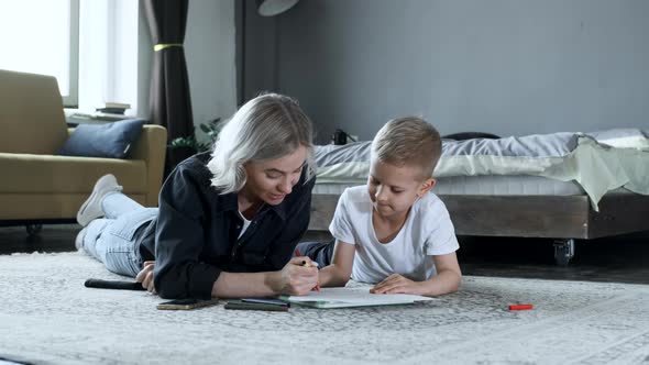 A Young Mother and A Baby Boy Are Sitting on the Floor, The Mother Is Teaching the Child To Draw