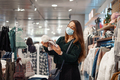 Young woman in face mask choosing warm hat in shopping mall - PhotoDune Item for Sale