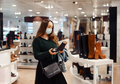 Young woman in face protective mask choosing boots in shoe department during covid-19 outbreak - PhotoDune Item for Sale