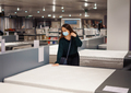 Pleasant young woman in medical face mask choosing new mattress in store during pandemic - PhotoDune Item for Sale