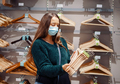 Young woman in face mask buying household products during pandemic, holding set of wooden hangers - PhotoDune Item for Sale
