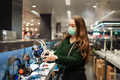 Young woman in medical face mask choosing modern headphones, shopping during Covid19 outbreak - PhotoDune Item for Sale
