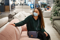 Young brunette female in face mask buying couch for home in shopping mall during covid-19 pandemic - PhotoDune Item for Sale