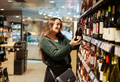 Happy young woman choosing favorite red wine standing by shelves in grocery store - PhotoDune Item for Sale