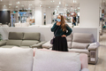 Young pensive woman in face mask standing in front of couch in furniture store department - PhotoDune Item for Sale