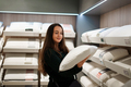 Cheerful brunette lady choosing new pillow while standing in bedding store - PhotoDune Item for Sale