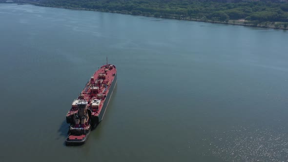 A drone view of a large red barge on the Hudson River in NY on a sunny day. The camera boom down and