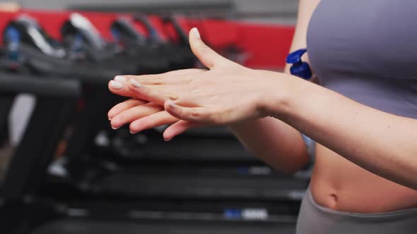Mid section of fit caucasian woman sanitizing her hands in the gym