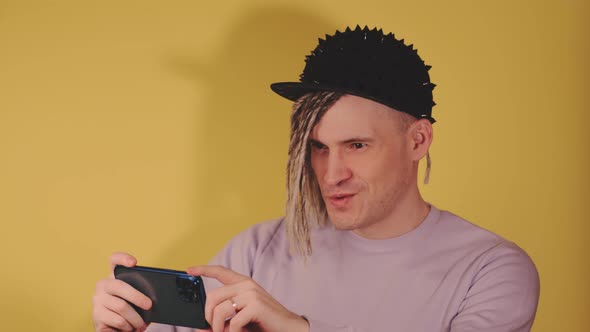 Young Handsome Man in Black Cap Taking Pictures on Mobile Phone on Yellow Background