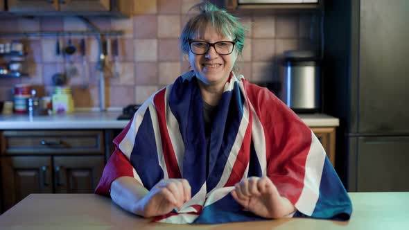 Caucasian adult woman wrapping in nationa british flag and smiling sitting at home.