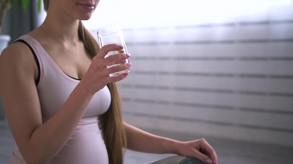 Pregnant Woman Drinking Water and Sitting on Floor During Yoga Practice in Apartment Room Spbd