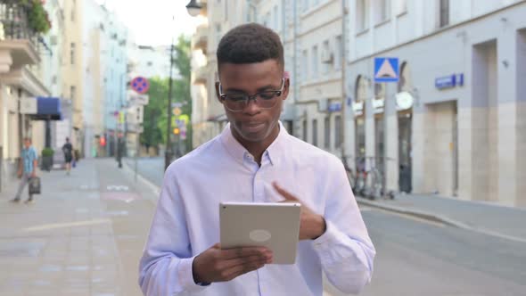 African Man Making Video Call on Tablet While Walking on the Street