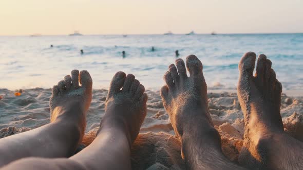 POV Feet of a Couple of Men and Women Lying on a Sandy Beach at Sunset By Ocean