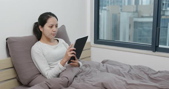 Woman study on tablet computer with apply paper mask on face at home