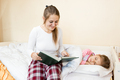young mother sitting on bed and reading bedtime story to daughter - PhotoDune Item for Sale