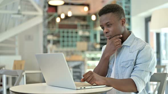 Pensive Young African Man Thinking and Working on Laptop in Cafe