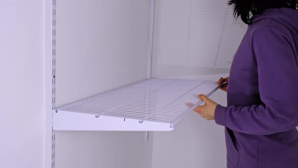 Installation of a metal mesh shelf in the dressing room system on a bracket. A woman in a purple hoo