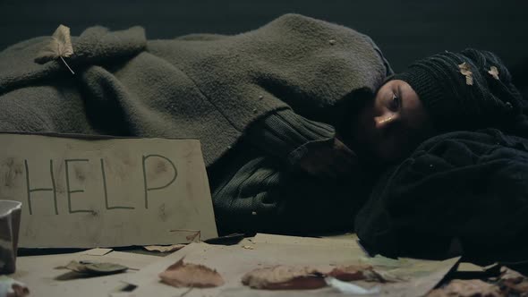 Homeless Bum With Help Sign on Board Lying in Dirty Place