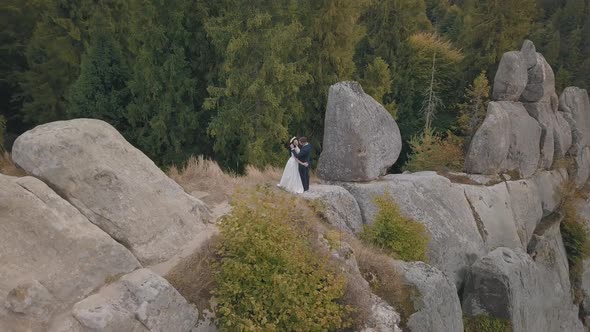 Newlyweds Stand on a High Slope of the Mountain. Groom and Bride. Aerial View