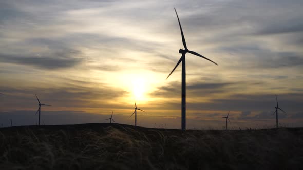 Motion the Blades of a Large Wind Turbine in a Field Against a Background of Orange Sunset on the