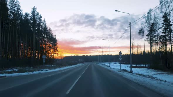 View Through the Windshield of a Moving Car on the Road in Winter and a Beautiful Sunrise in the Sky