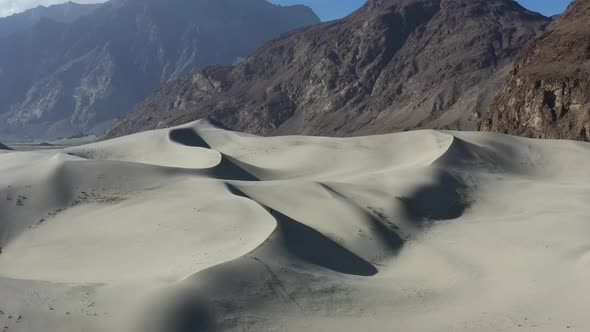 aerial drone flying past sand dunes in the Cold Desert of Skardu Pakistan with the rugged mountain r