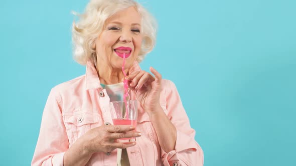 Friendly Cool Grandmother Holding a Glass and Tasting Juice