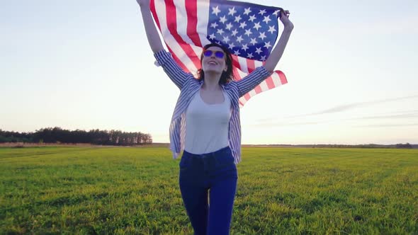 Young Positive Woman with an USA Flag Runs Across a Field at Sunset Slow Mo