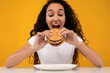 nk Food Posing With Open Mouth Over Yellow Orange Studio Background. Woman Enjoying Hamburger. Unhealthy Nutrition And Binge Eating Habit Concept