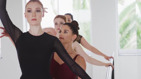 Caucasian ballet female dancers exercising with a barre by a mirror during a ballet class