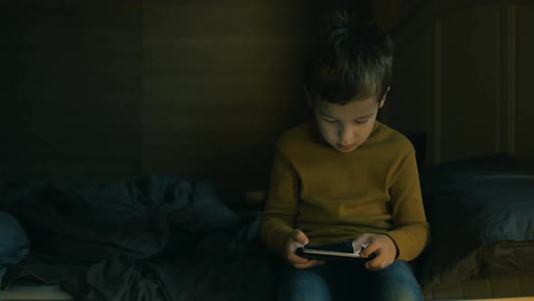 Child with Cellphone Sitting on Bed at Home