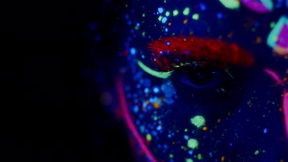 Young woman in bright fluorescent makeup glowing under UV light. Closeup of her eye opening and clos
