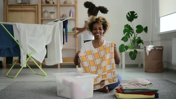 African Woman Folding Clean Clothing From Clothes Dryer in Basket Spbd