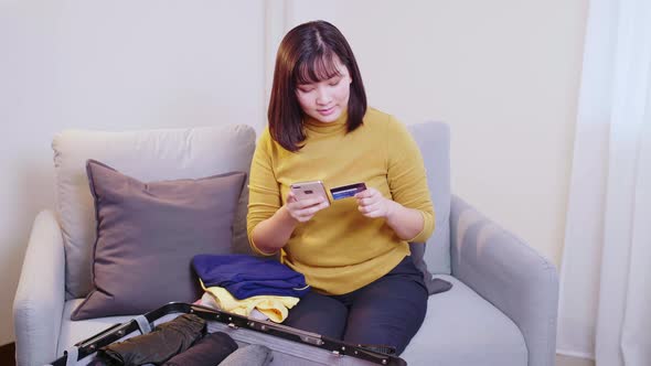 Beautiful Asian woman booking online with her cell phone and credit card for travel in the summertim