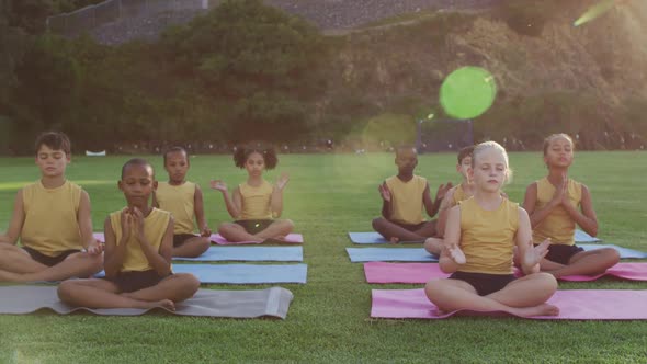 Diverse group of schoolchildren sitting on mats meditating during yoga lesson outdoors