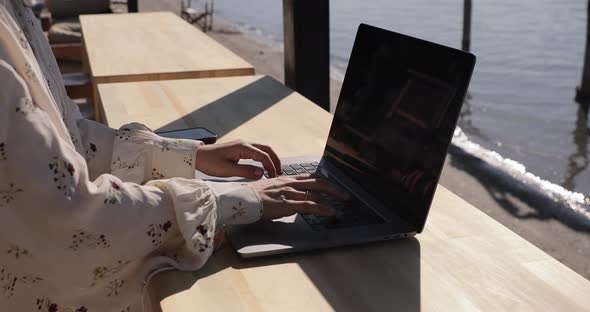 Student typing on laptop. Sea beach hotel resort background