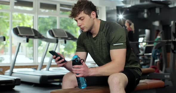 Portrait of Confident Bodybuilder Looking Phone Screen at Gym