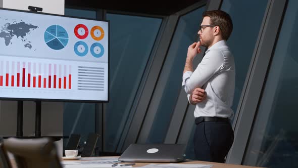 Thinking young man looking at screen with analytics in meeting room