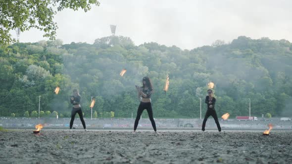 Young Slim Man and Two Beautiful Women Simultaneously Perform Show with Flame While Standing