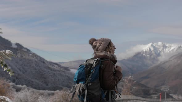 A Girl with a Hiking Backpack Walks Along the Road in the Winter Mountains of the Alps