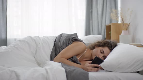 Young Woman Using Smartphone before Sleeping in Bed