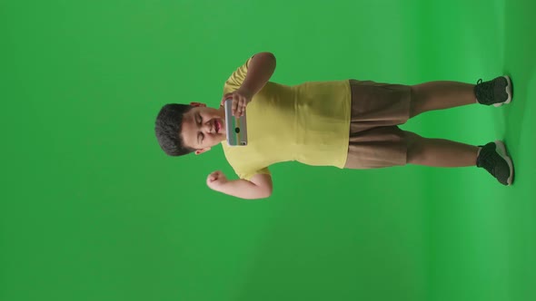 Full Body Of Excited Asian Little Boy Playing Video Game With Phone And Celebrating In Green Screen