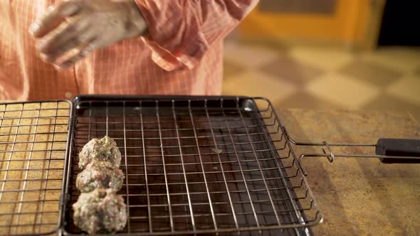 Man rolls balls of kofta in his hand and puts into grilling basket for cooking.  Camera slides from