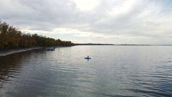 Person sitting in a blue kayak, paddling slowly along the shoreline of buffalo lake, Alberta. Slow a