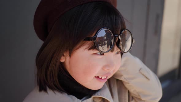 Korean Girl in a Gray Coat and Cap Stands the Street in Spring at the Glass Doors of the Store